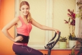 Active young woman working out on exercise bike stationary bicycle. Sporty girl training at home listening music. Fitness and weight loss concept.