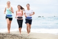Running friends on beach jogging group training. Exercising runners training outdoors living healthy active lifestyle. Multiracial fitness runner people working out together outside smiling happy.