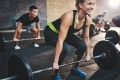 Cheerful muscular young woman with ponytail and black tights performing dead lift barbell exercises with other students